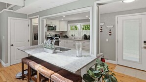 A modern kitchen with a central island, white cabinetry, and a view of the outdoors. - Shore House 003-DP Newly renovated in Dennis Port, 2 minute walk to the beach! (Dennis Port)