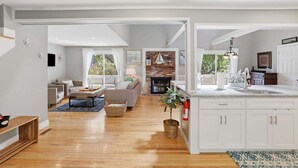 A modern kitchen with white cabinetry, a central island, and a fireplace. - Shore House 003-DP Newly renovated in Dennis Port, 2 minute walk to the beach! (Dennis Port)