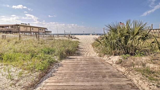 A wooden boardwalk leading to a beach with a building on stilts and an American flag. - Gulf Shores Home w/ Shared Pool, 2 Blocks to Beach (Gulf Shores)