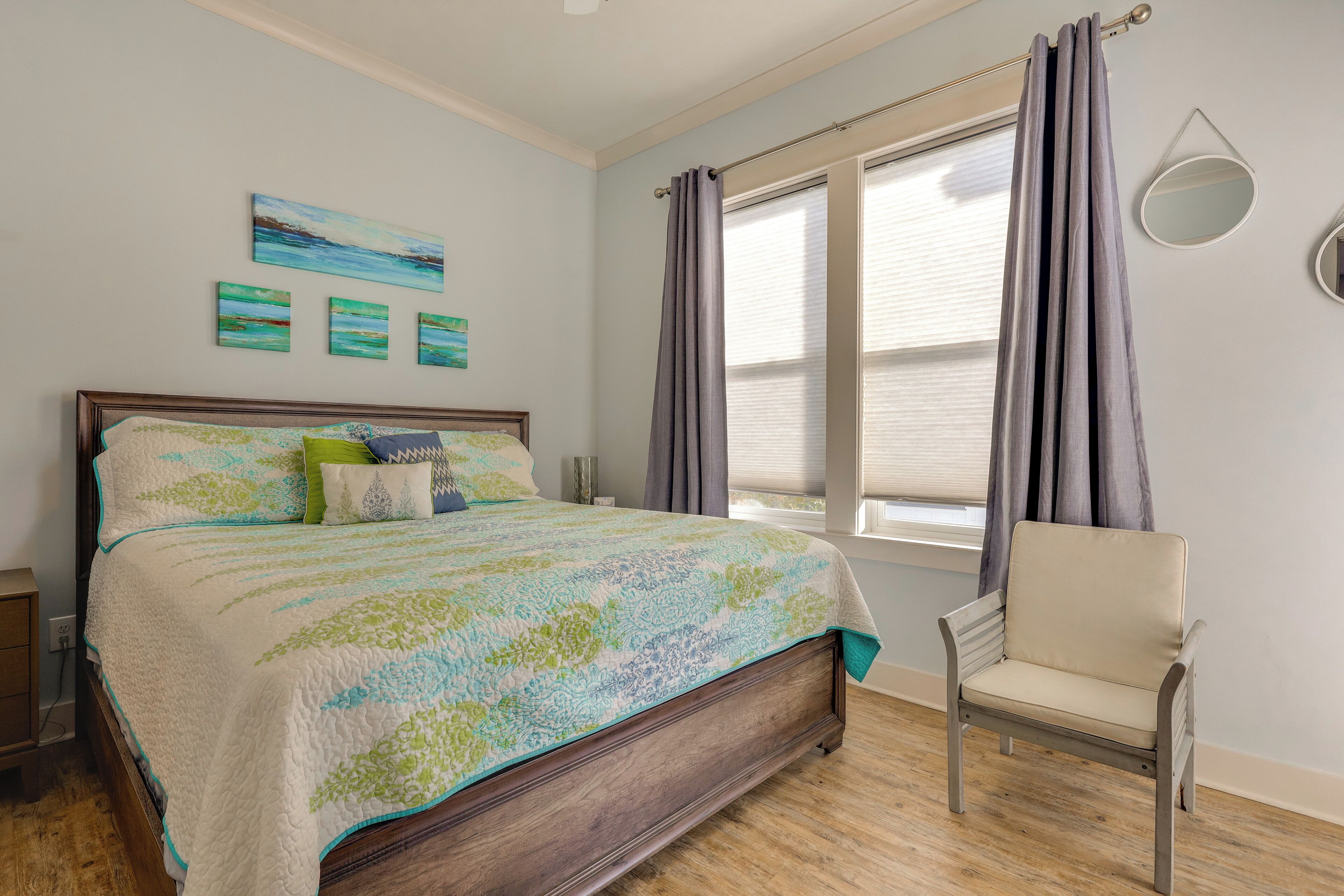 A bedroom with a bed, a chair, a window with curtains, and wall art.