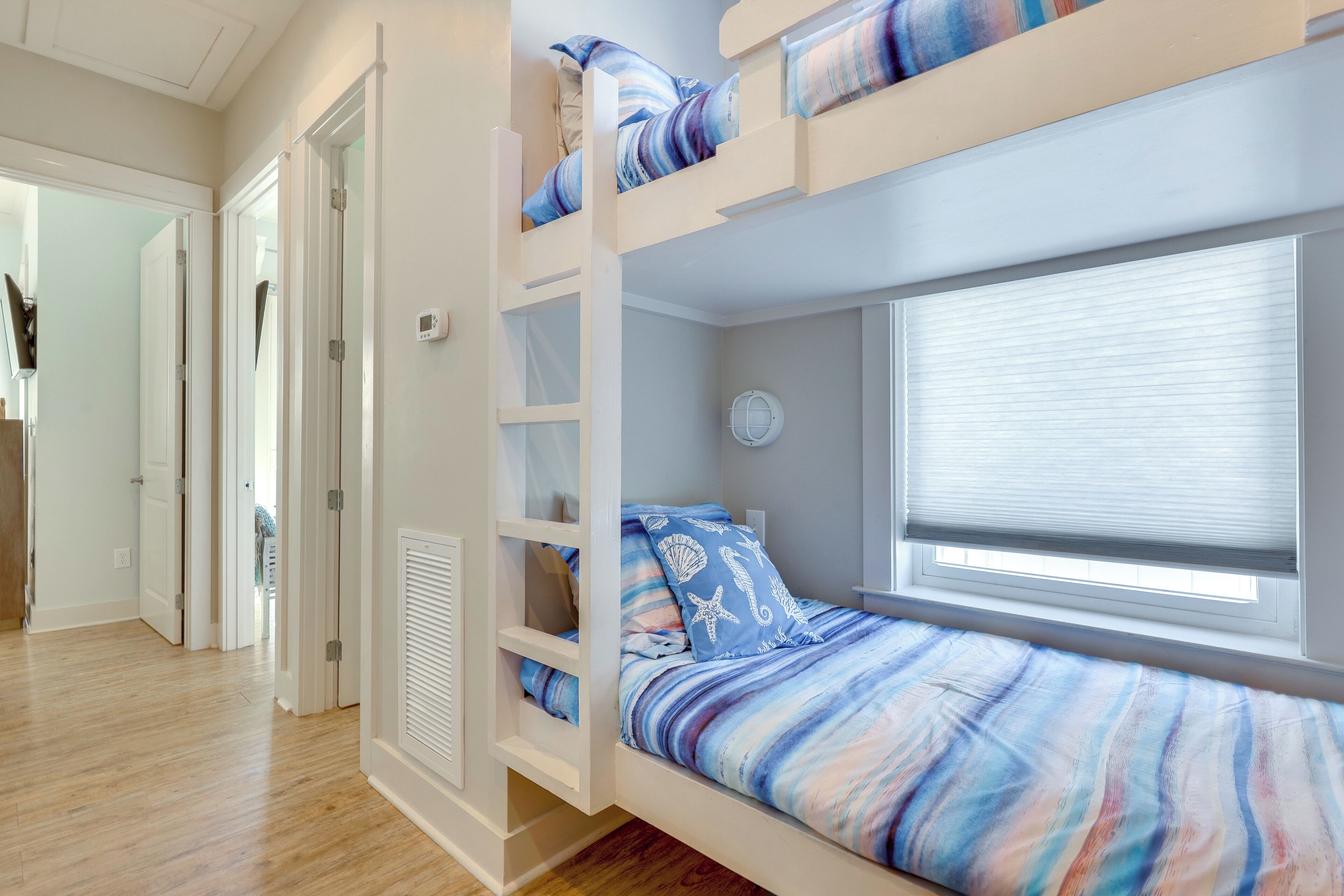 Une chambre avec un lit superposé, une fenêtre, une porte et une armoire blanche.