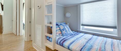 Une chambre avec un lit superposé, une fenêtre, une porte et une armoire blanche.