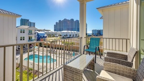 A balcony with wicker furniture overlooking a swimming pool and a view of high-rise buildings. - Gulf Shores Home w/ Shared Pool, 2 Blocks to Beach (Gulf Shores)