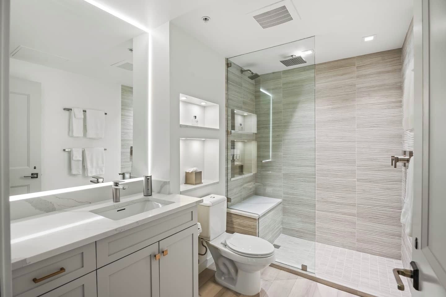 A modern bathroom with a glass shower enclosure, a large mirror, and a vanity with a sink and cabinet.