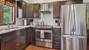 A modern kitchen with stainless steel appliances, wooden cabinets, and a window with curtains. - Lone Bear Cabin: EV, River Access, Mountain Views, Fireplace, Hot Tub (Rileyville)