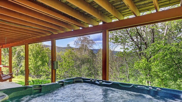 A hot tub under a wooden pergola with a view of a forested area. - Lone Bear Cabin: EV, River Access, Mountain Views, Fireplace, Hot Tub (Rileyville)