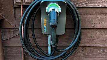 A garden hose coiled and attached to a wall-mounted electrical outlet with a red cap and a label reading "TELEPHONE NETWORK INTERFACE."