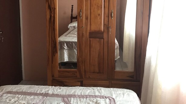 A bedroom with a large bed, wooden wardrobe, and a mirror cabinet. - Laura's Place (Port Antonio)