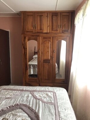 A bedroom with a large bed, wooden wardrobe, and a mirror cabinet. - Laura's Place (Port Antonio)