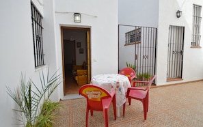 A small outdoor patio with a table and chairs, a door leading to a room, and a tiled floor.