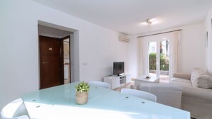 Un salon moderne avec une table à manger en verre, un canapé, un téléviseur et un petit balcon.