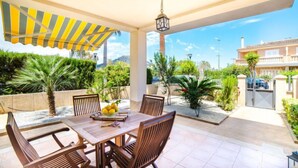 Une terrasse couverte avec une table et des chaises, un auvent à rayures jaunes et une vue sur un quartier résidentiel avec une porte et une voiture garée.