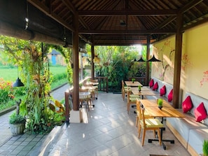 Un espace de restauration en plein air avec des tables et des chaises en bois, entouré de verdure et doté d’un sol carrelé.