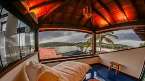 Una habitación con cama, un taburete pequeño y vistas a un paisaje costero.
