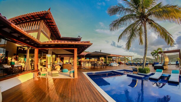 Una terraza de madera con piscina, sillones de descanso y zona de bar.