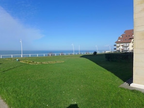 A grassy area with a white fence and a building with balconies, overlooking a body of water. - La Bizontine by Interhome (Cabourg)