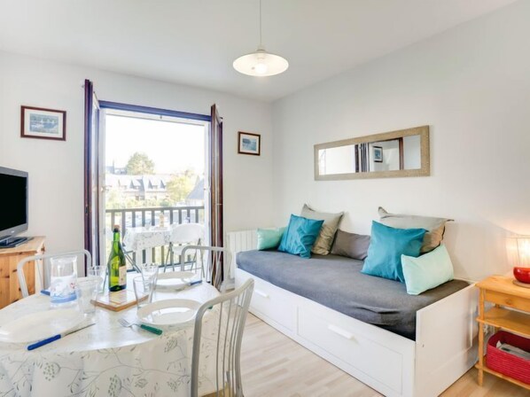 Una habitación acogedora con sofá cama, una mesa de comedor con sillas, un televisor y un ventanal con vistas a edificios.