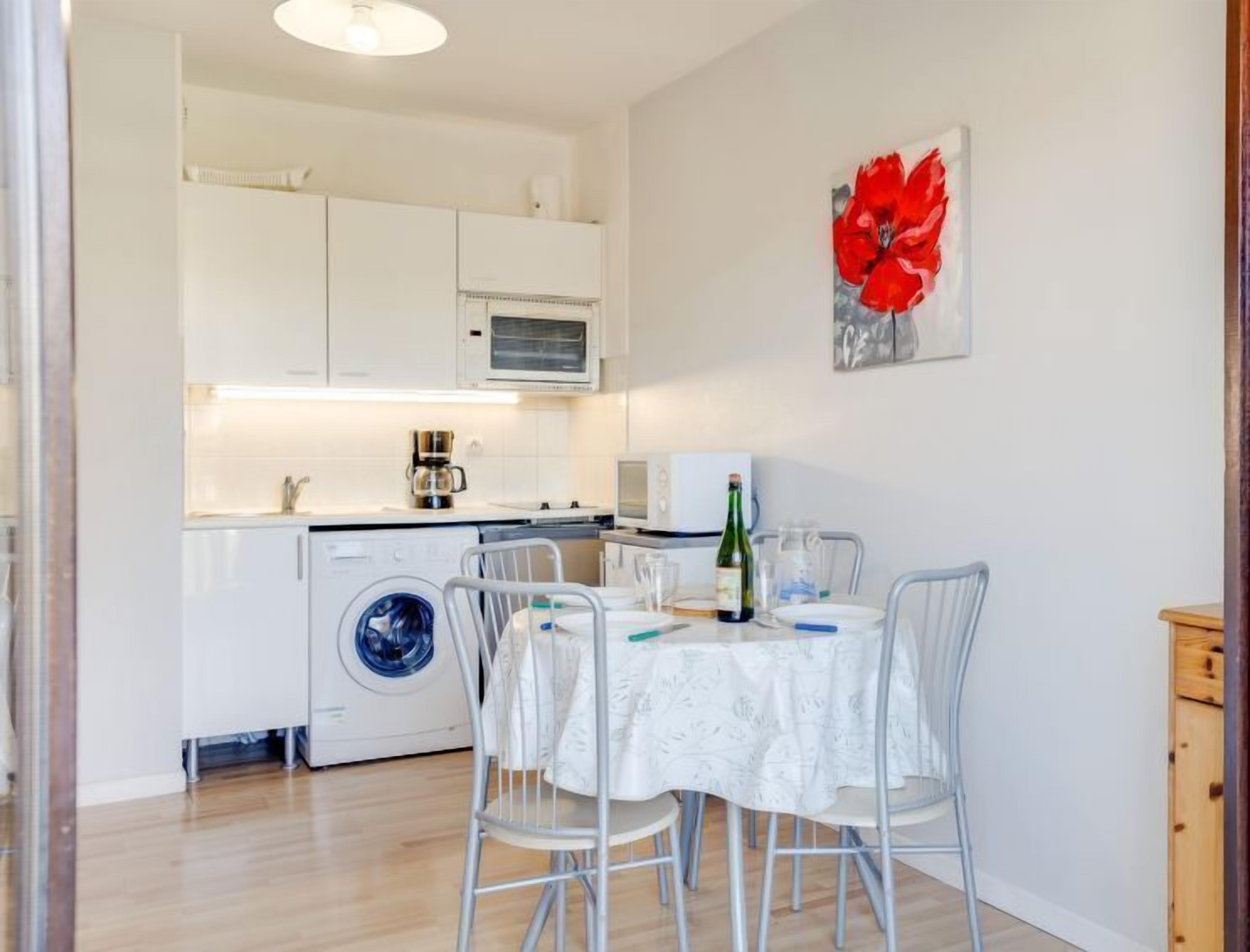 Une cuisine compacte avec des meubles blancs, un lave-linge et un coin repas comprenant une table et des chaises.