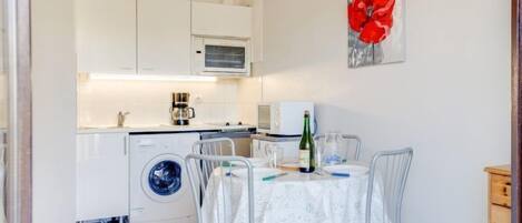 Une cuisine compacte avec des meubles blancs, un lave-linge et un coin repas comprenant une table et des chaises.