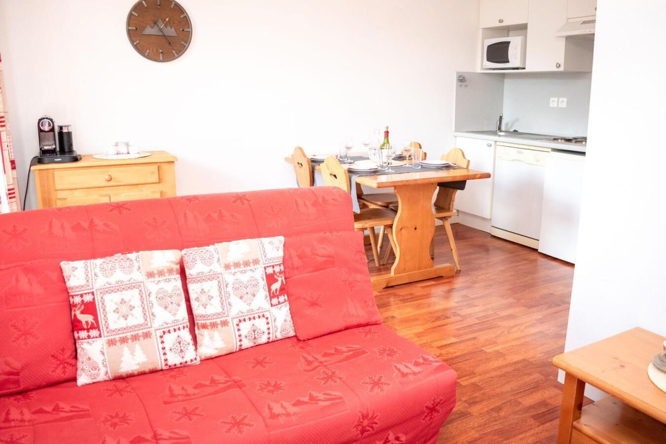 Ein gemütlicher Wohnbereich mit einem roten Sofa, einem Holzesstisch und einer Küche im Hintergrund.