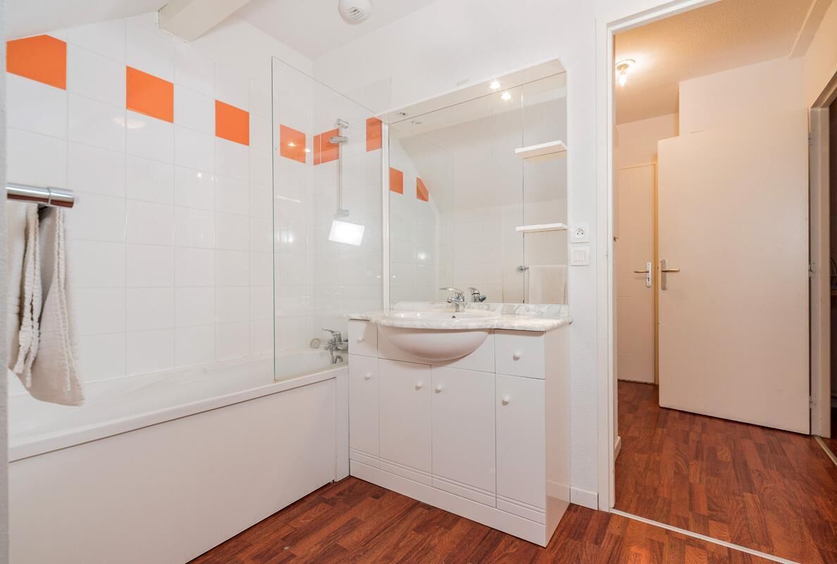 Une salle de bain moderne avec un lavabo blanc, un miroir et un revêtement de sol en bois.