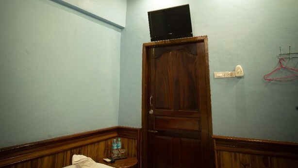 A room with a wooden ceiling, a bed with two towels, a wooden door, and a wall-mounted TV. - Salakphet Guesthouse (Luang Prabang)