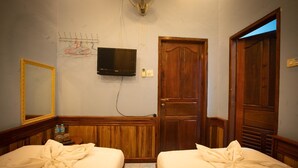 A hotel room with two beds, a television mounted on the wall, a wooden door, and a mirror on the wall. - Salakphet Guesthouse (Luang Prabang)