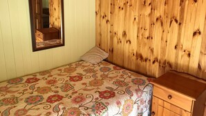 A bedroom with a bed, a wooden wardrobe, a mirror, and a floral bedspread.