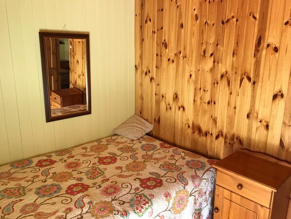A bedroom with a bed, a wooden wardrobe, a mirror, and a floral bedspread.