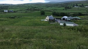 A rural landscape with rolling hills, a farmhouse, and a small cluster of buildings with green roofs.