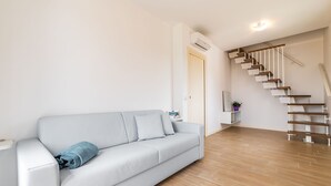 Un salon moderne avec un canapé gris clair, un plancher en bois, un mur blanc et un escalier en bois.