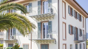 Un immeuble à plusieurs étages doté de balcons, de fenêtres avec volets et d’un palmier au premier plan.