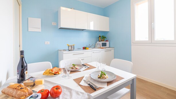 Une cuisine moderne avec des meubles blancs, une table à manger dressée avec des assiettes remplies de nourriture et une fenêtre laissant entrer la lumière naturelle.