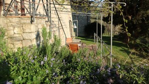 Un bâtiment en pierre doté d’un espace jardin, comprenant une pergola couverte de plantes grimpantes, une table en bois et des chaises.