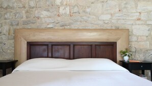 Un lit avec une tête de lit en bois adossée à un mur en pierre.