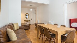 A modern living room with a wooden dining table, leather sofa, and a red bed. - Victoria Best Apartments # 3 (Athina)