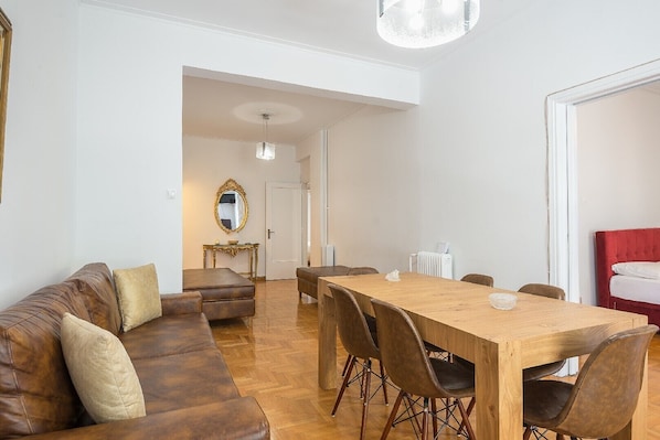 Ein modernes Wohnzimmer mit Esstisch aus Holz, einer Ledersofa und einem roten Bett.