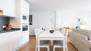 Una cocina moderna con armarios blancos, una mesa de comedor con sillas y un sofá beige en una sala de estar luminosa y minimalista.