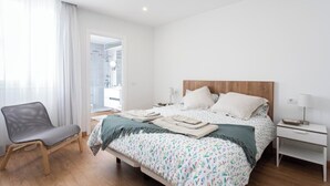 Un dormitorio moderno con cabecera de madera, cama con ropa de cama estampada, mesita de noche con lámpara y una silla.