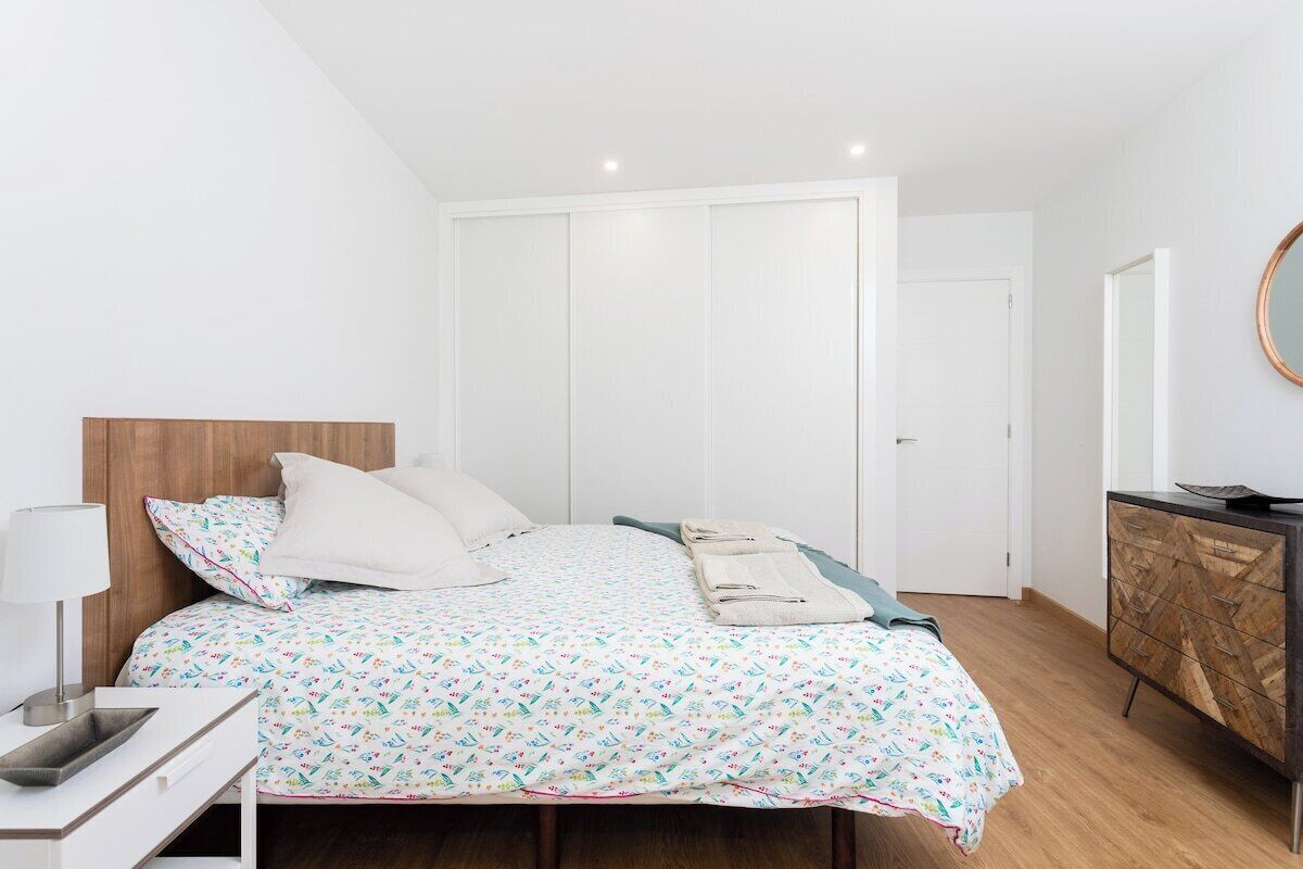 Et soveværelse med seng, sengebord, lampe, garderobeskab og et spejl på væggen.