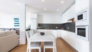 Una cocina moderna con armarios blancos, una mesa de comedor con sillas y un horno empotrado.