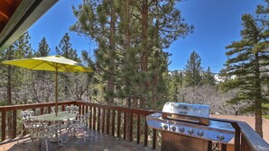 A wooden deck with a grill, outdoor table and chairs, and a yellow umbrella.