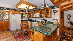 A rustic kitchen with wooden cabinets, a central island, a hanging light fixture, and a window with a view of trees.