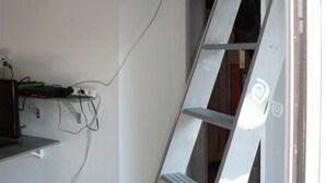 A room with a white wall, a ladder, and a television on a stand.
