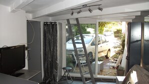 A compact living space with a TV, a couch, a ladder, and a view of a parked car through a glass door.