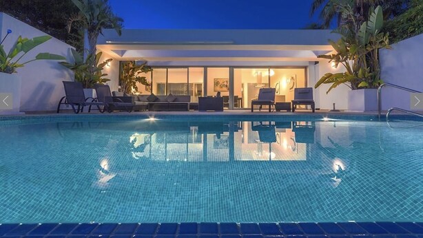 Et moderne hotel med swimmingpool, liggestole og tropiske planter.