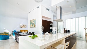 Et moderne køkken med en central ø, et spiseområde med stole, og en stue med sofa og et billede.