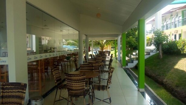 An outdoor cafe area with wicker chairs and tables, a glass wall with a view of the street, and a green railing along the edge.