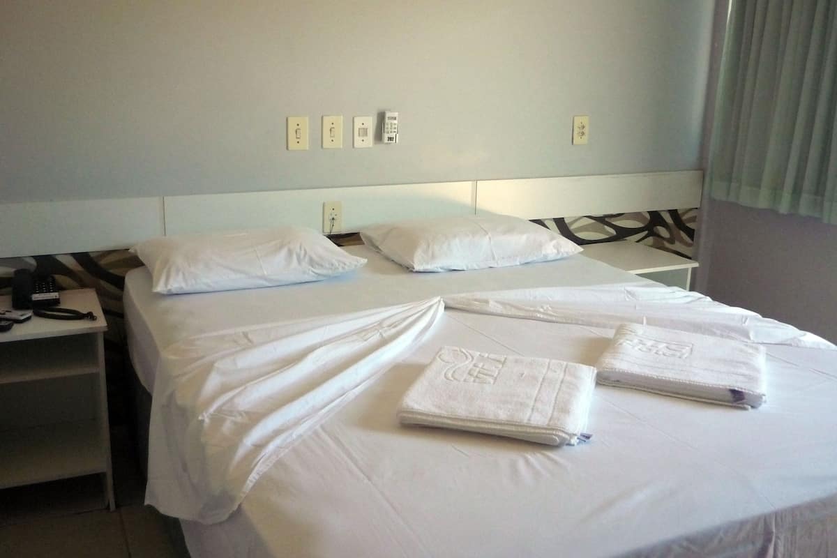 A hotel room with two beds, white linens, a bedside table with a phone, and a wall with four light switches.