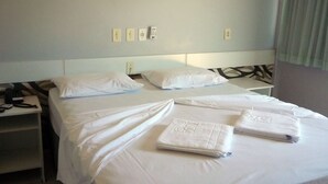 A hotel room with two beds, white linens, a bedside table with a phone, and a wall with four light switches.